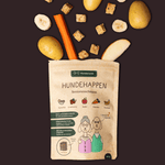 Hunderunde Hundehappen Seniorenschmaus Leckerli-Tüte mit Zutaten (Kartoffel, Karotte, Banane, Apfel) und Leckerli-Würfeln auf dunklem Hintergrund.