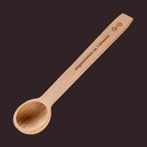 The Portionierer - fasst ca. 1 g vom Topping features "Abgestrichen ca. 1 Gramm" engraved on its wooden handle, pictured against a dark background.